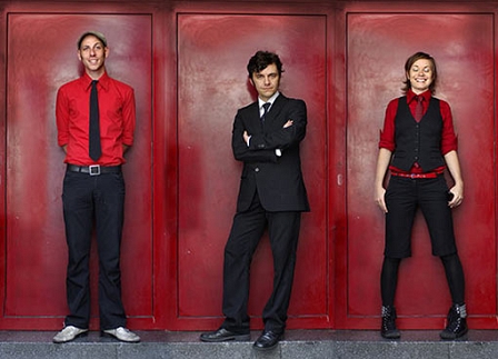 Die Band Angelika Express, in elegantes schwarz und rot gekleidet, vor einer roten Wand.